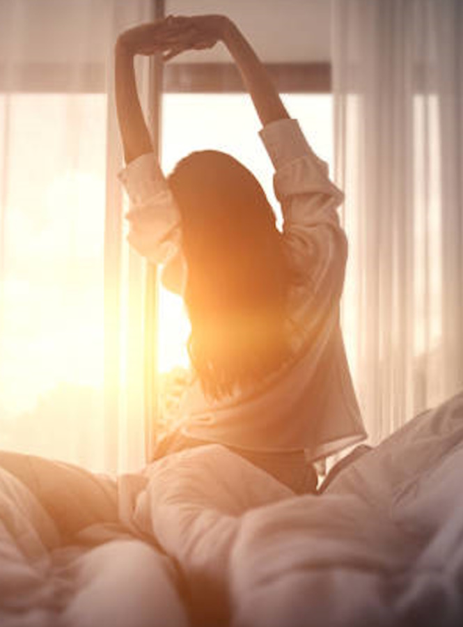 Happy woman stretching in bed after waking up.